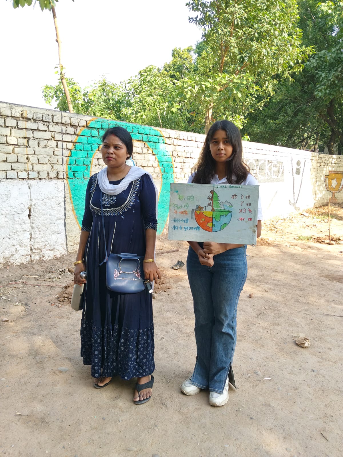 A volunteer and student holding a hand-painted environment awareness poster